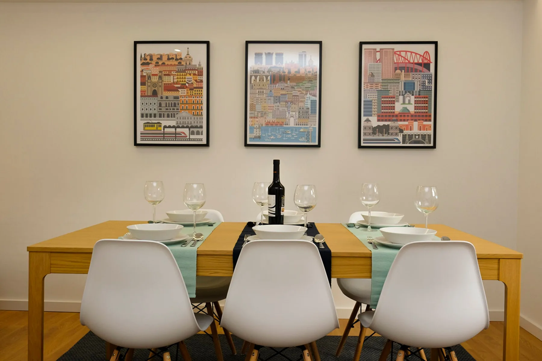 Comedor con una mesa de madera, asientos blancos y láminas enmarcadas en la pared.