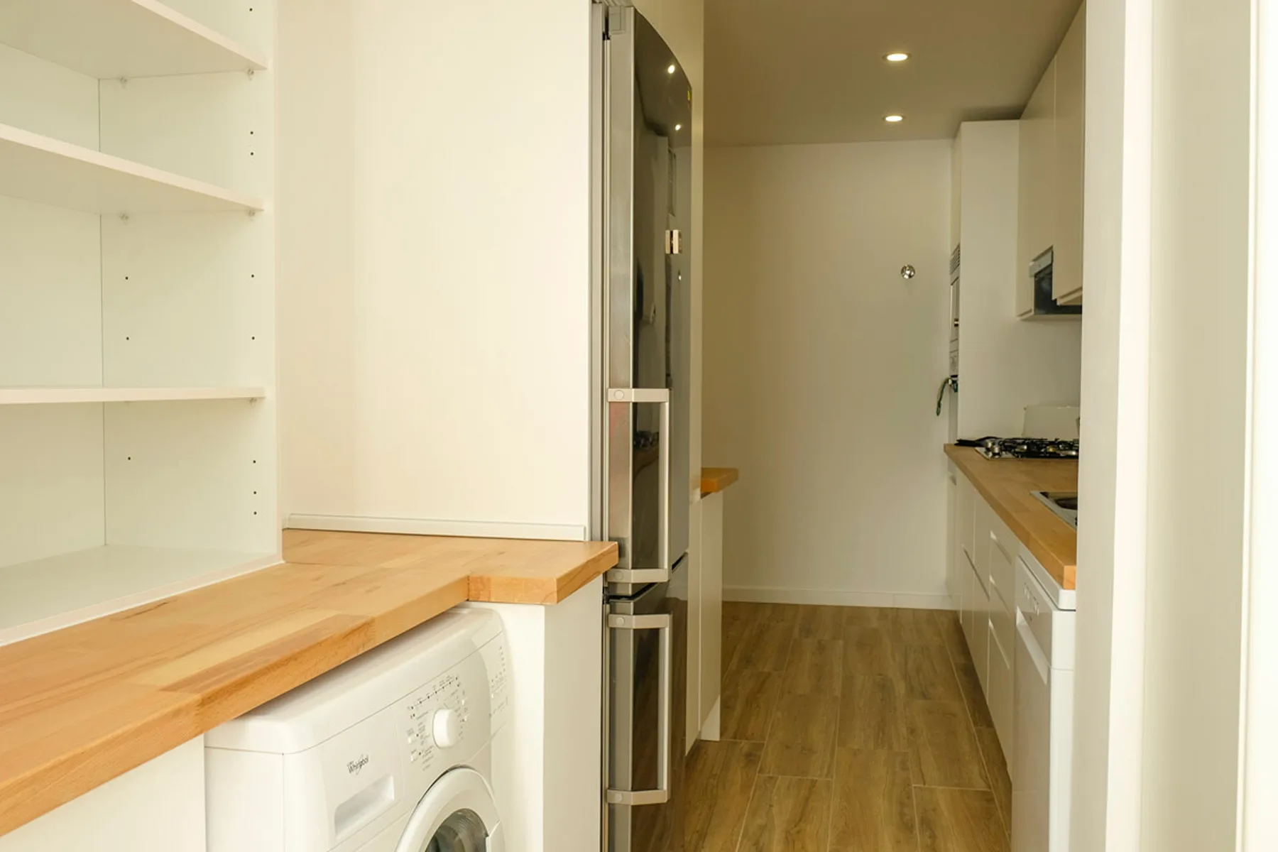 Una cocina estrecha con encimeras de madera, armarios blancos y una lavadora.