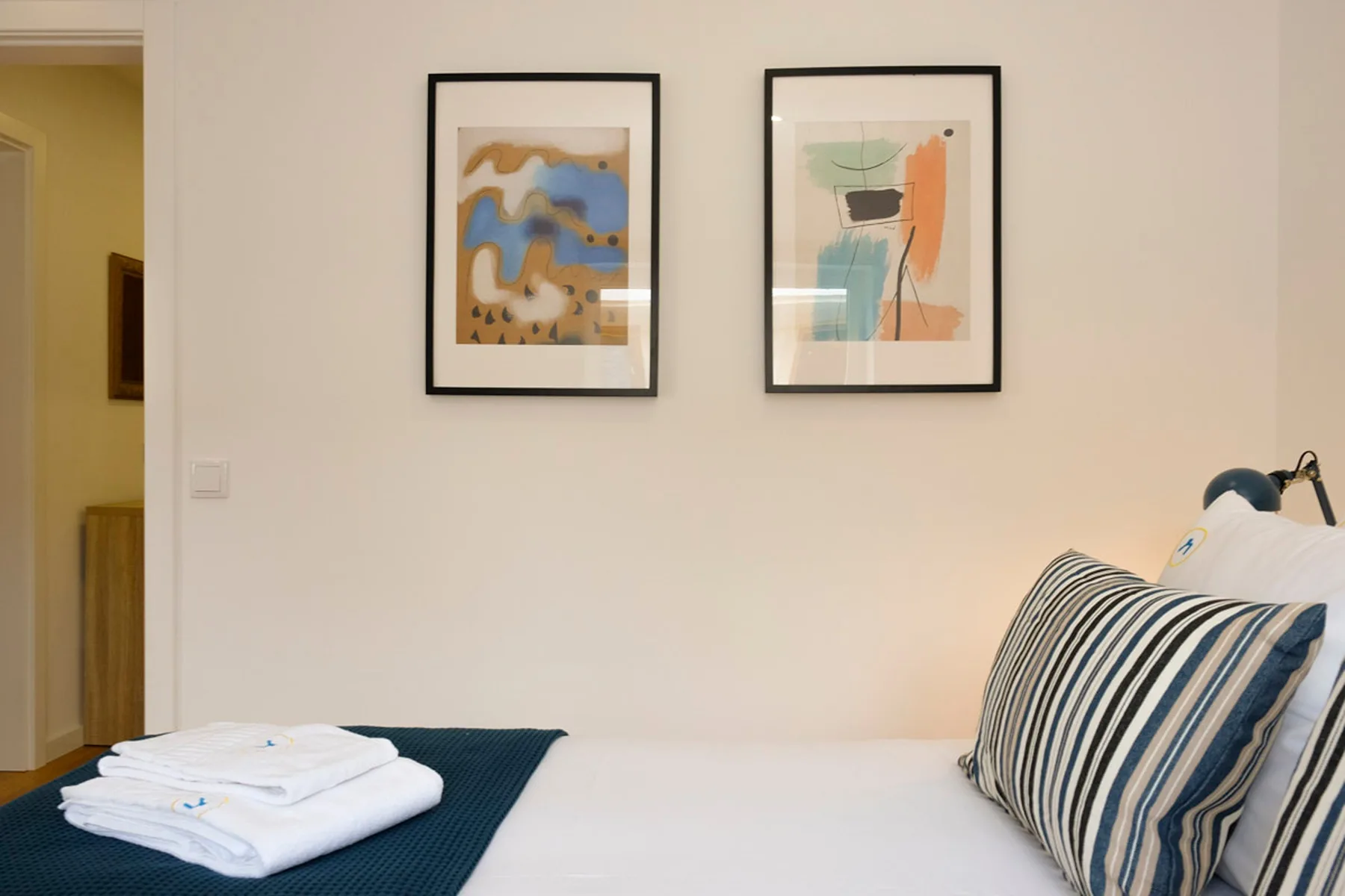 Un dormitorio con una cama bien arreglada y dos láminas enmarcadas en la pared.