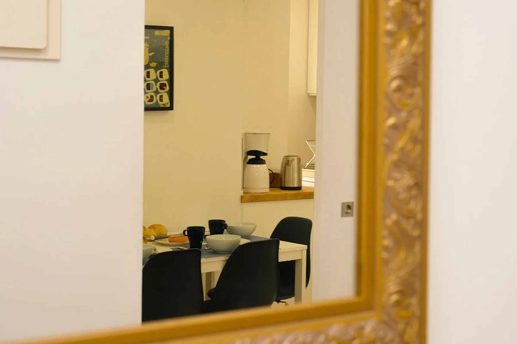 Un comedor con una mesa, asientos oscuros y pequeños electrodomésticos sobre una encimera.