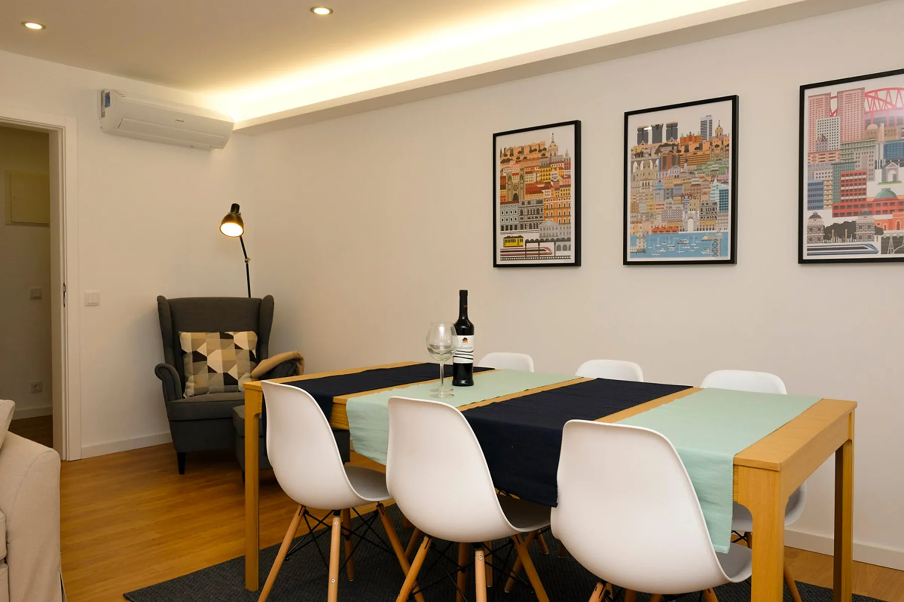 Comedor con una mesa, asientos blancos y láminas enmarcadas.
