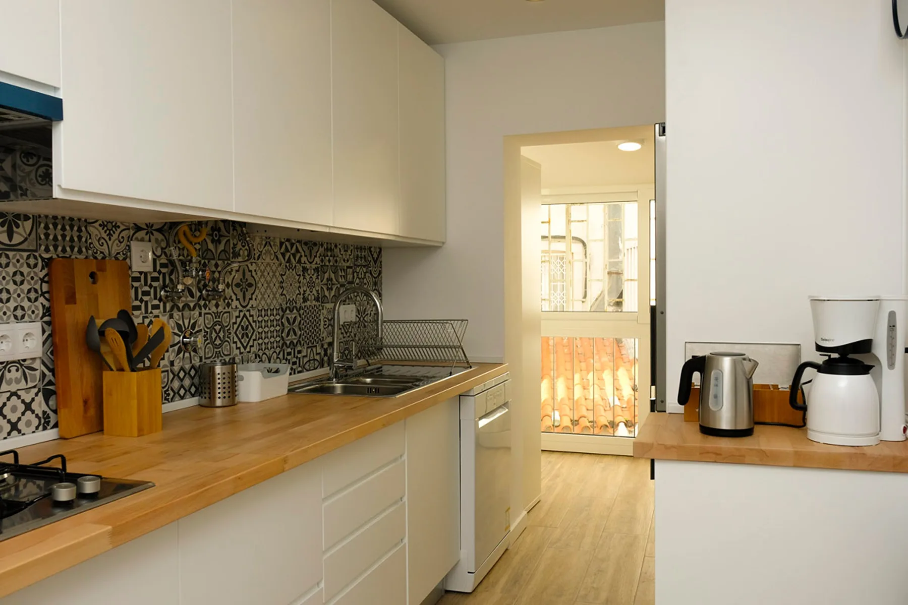 Una cocina luminosa con encimeras de madera, un salpicadero estampado y una puerta hacia un balcón.