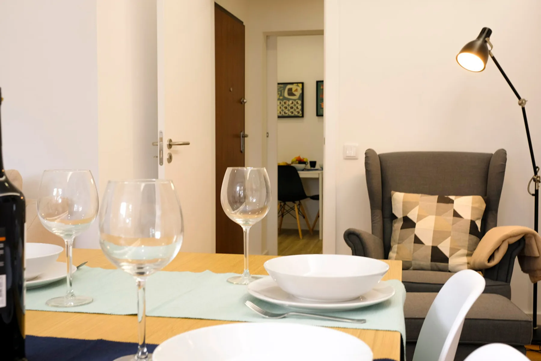 Una mesa de comedor con vajilla está junto a una sala de estar con un sillón y una lámpara de pie.