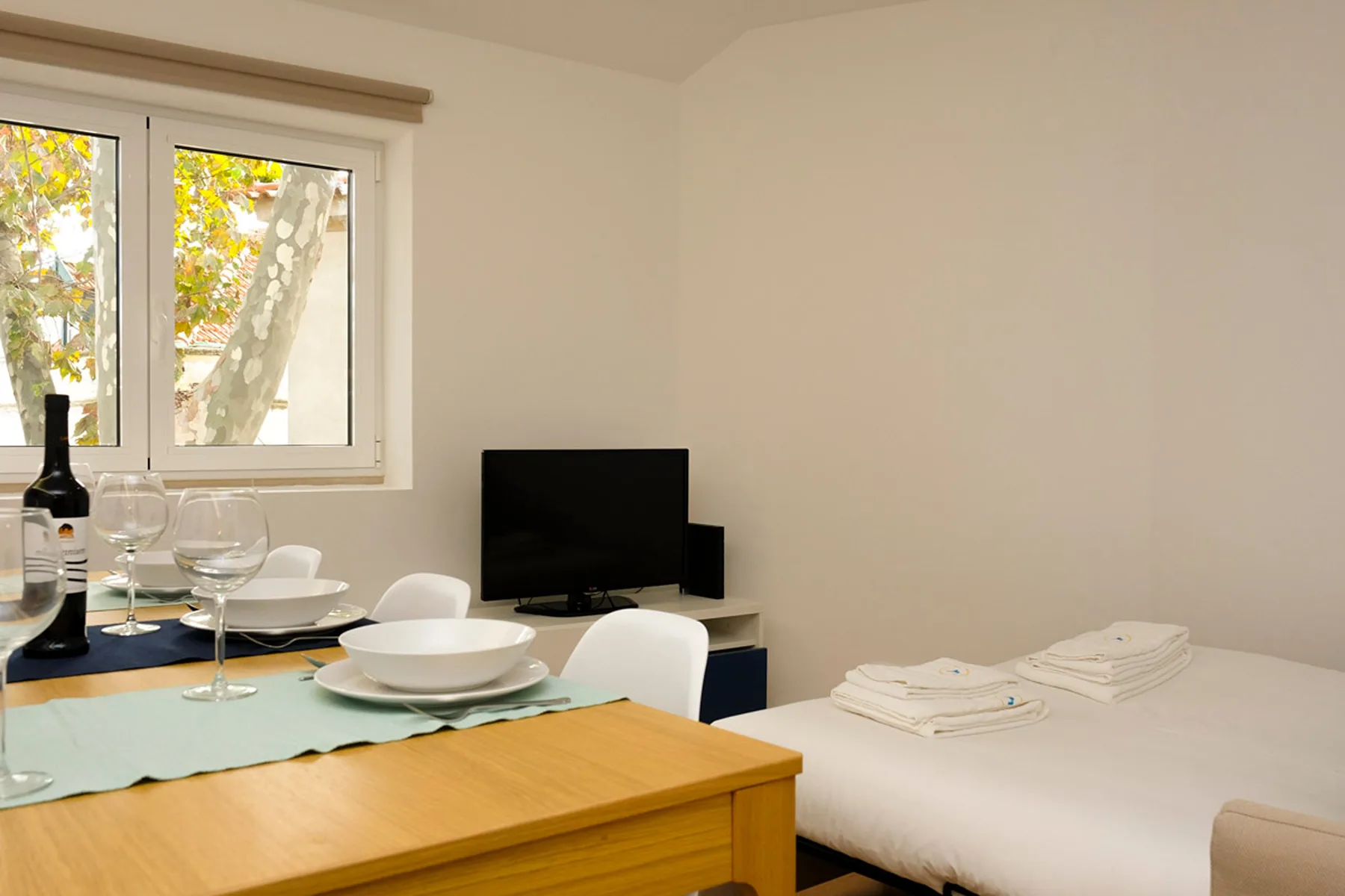 Un comedor y una cama comparten una habitación luminosa junto a una ventana.