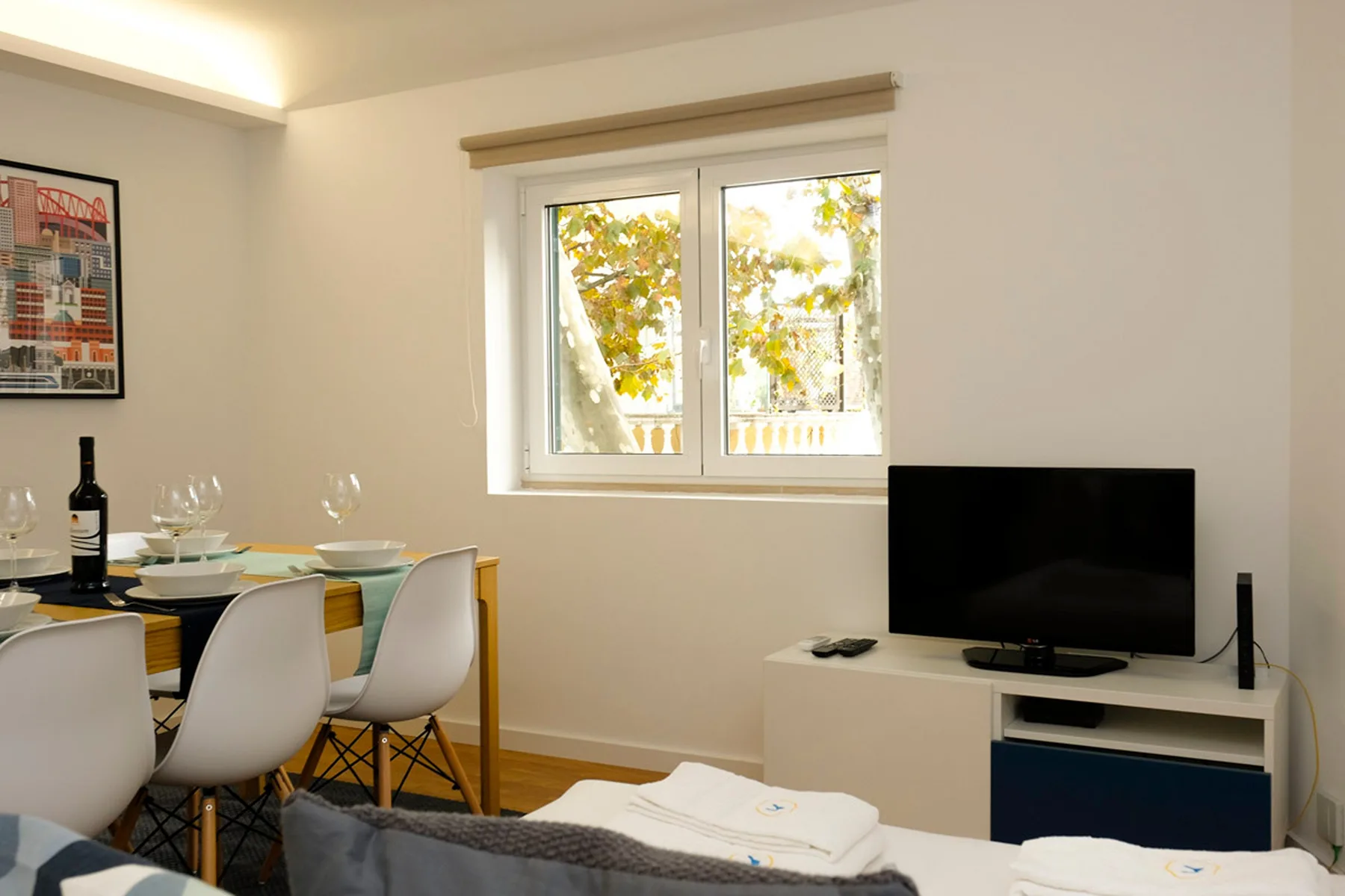 Dormitorio con cama, mesa de comedor y televisor junto a una ventana.
