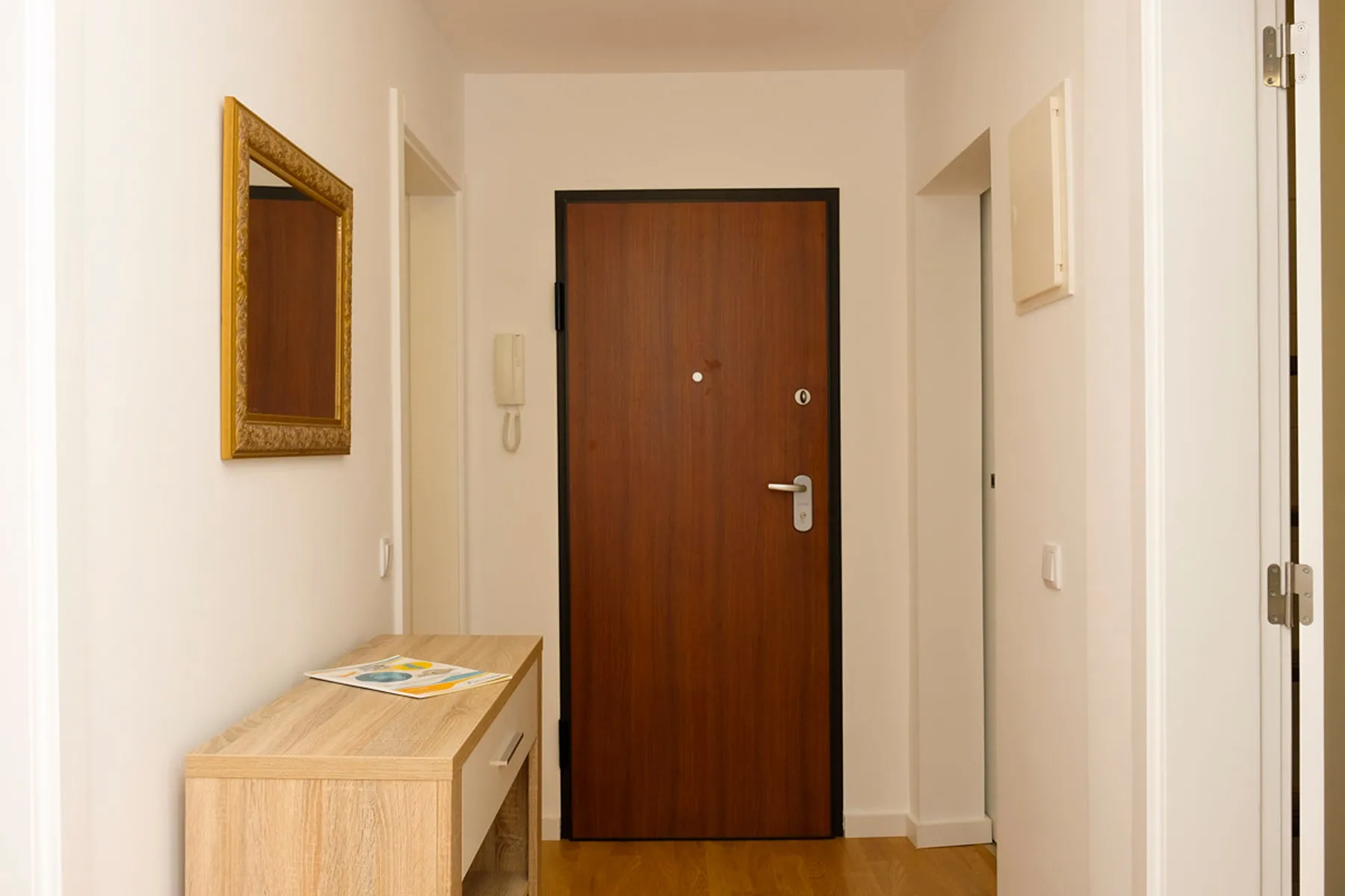 La entrada de un apartamento con una puerta de madera y una pequeña consola.