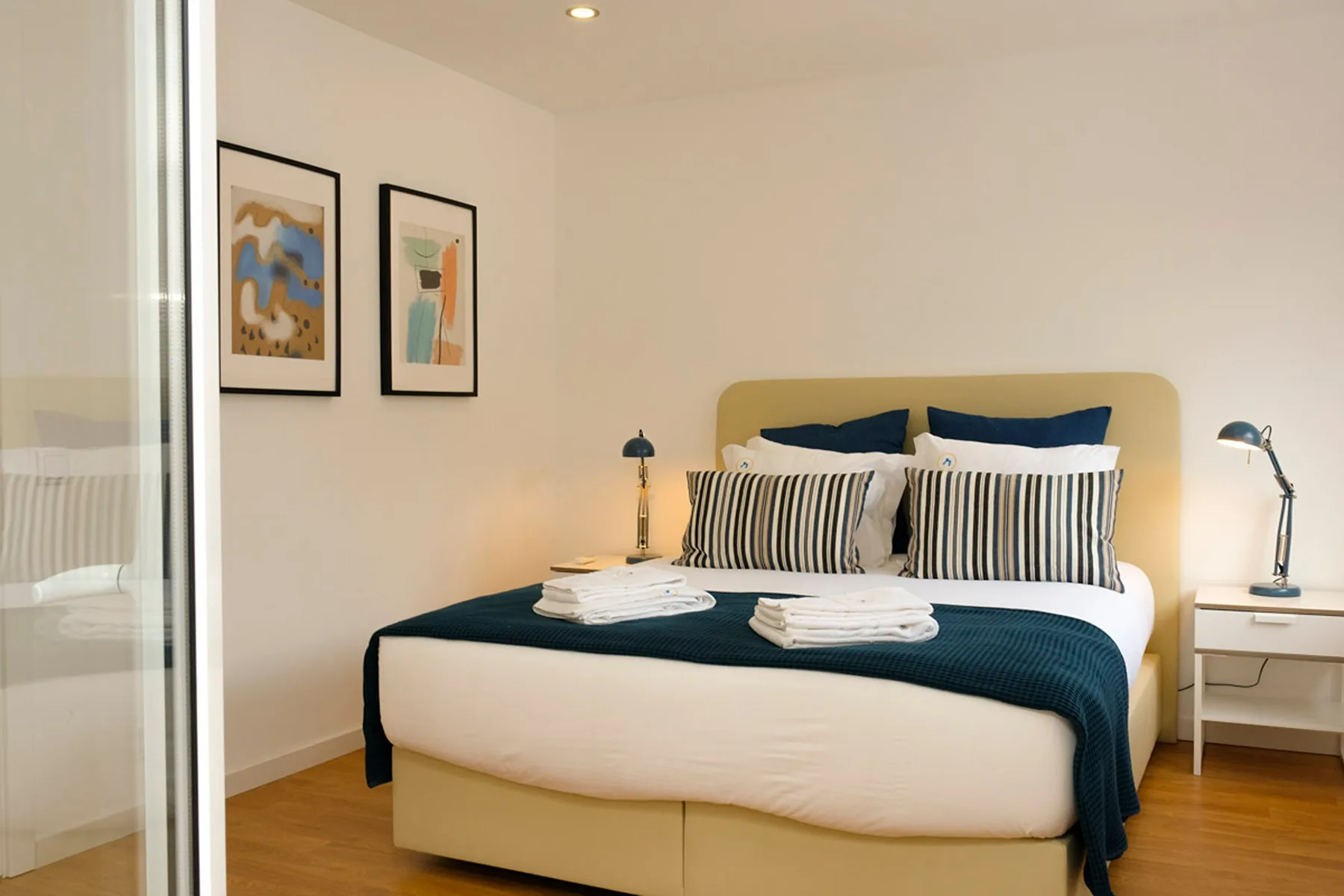 Dormitorio con una cama tendida, cojines a rayas y cuadros en la pared.