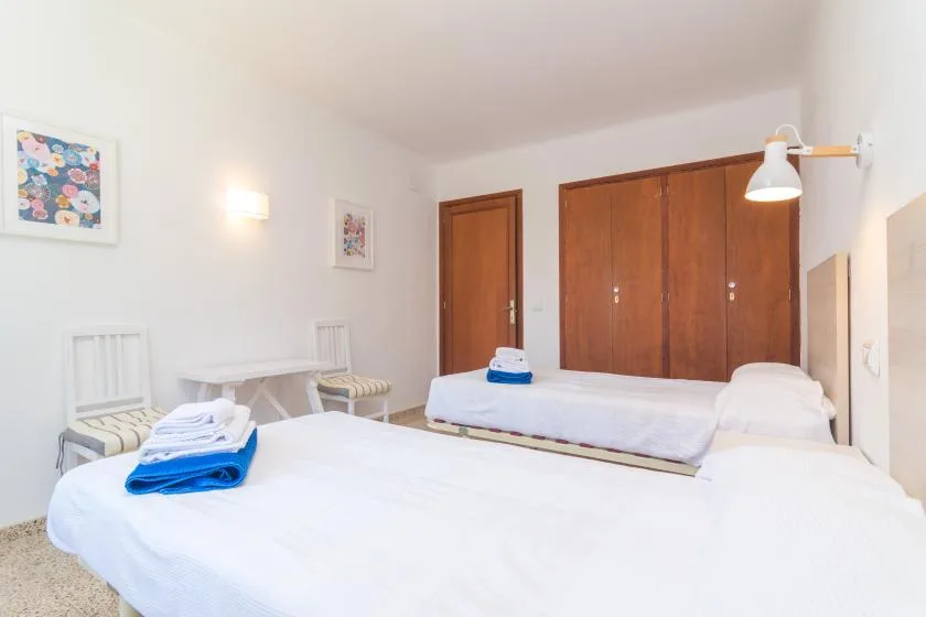 A bright bedroom with white bedding, wooden wardrobes, and small framed pictures.