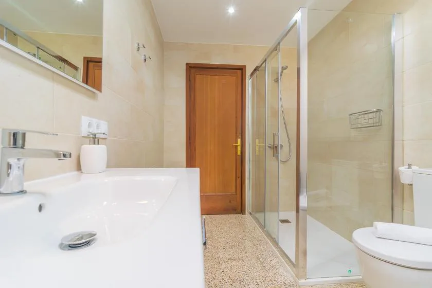 A tiled bathroom with a glass shower, sink, and wooden door.