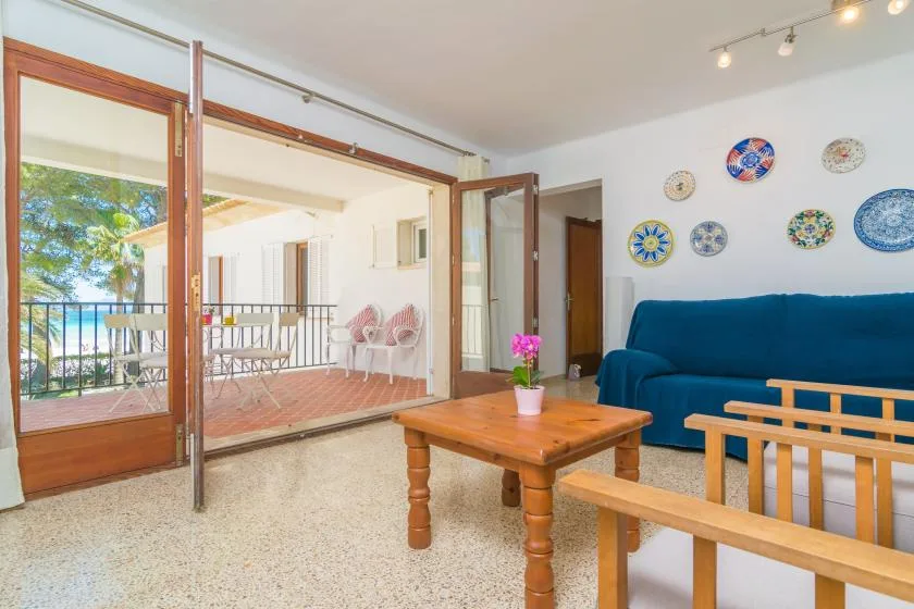 A living room with blue seating, a wooden coffee table, and open doors to a terrace.