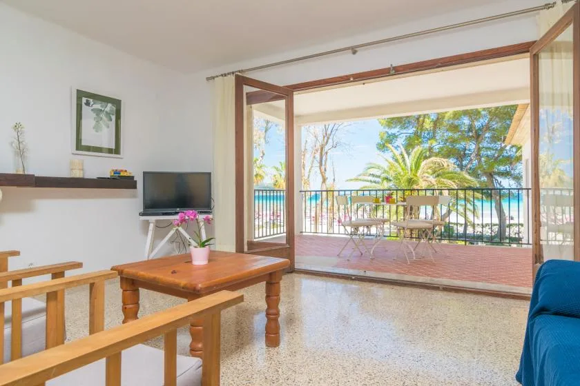 A bright living room opens onto a balcony with outdoor seating and leafy trees.