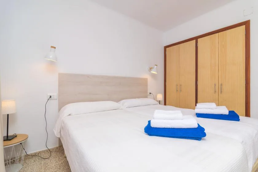 A bedroom with white beds and folded towels in front of a wooden wardrobe.