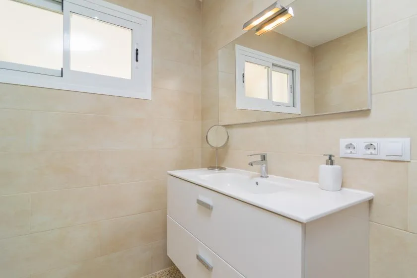 A bathroom vanity with a wide mirror and a small window.