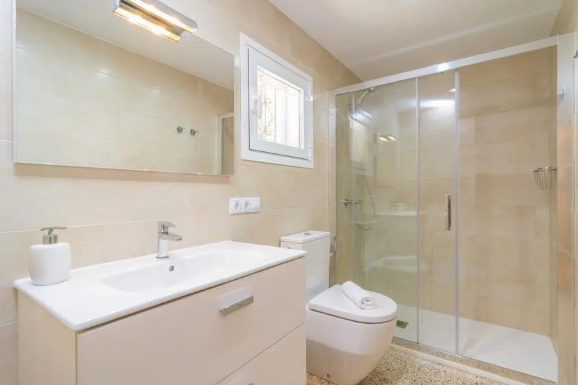 A bright bathroom with a vanity, toilet, and glass-enclosed shower.