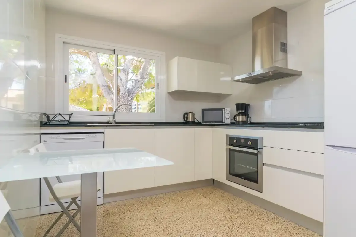 A bright kitchen with white cabinets, dark countertops, and a window.