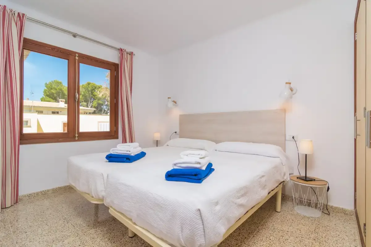 A bright bedroom with a bed dressed in white linens beside a window.