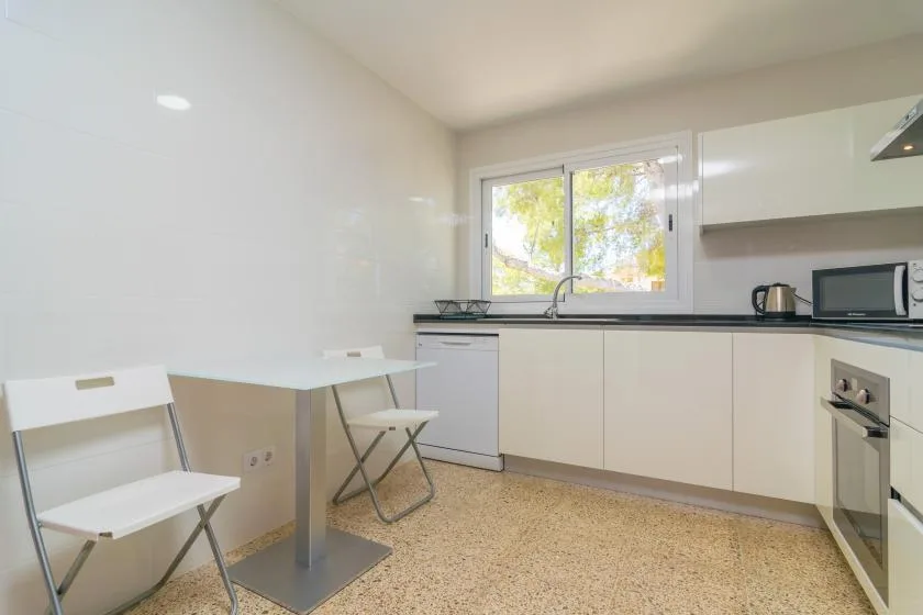 A bright kitchen with white cabinets, a window, and a small dining table.