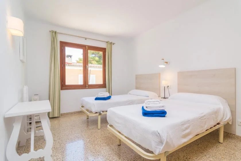 A bright bedroom has two beds with white linens and folded towels.