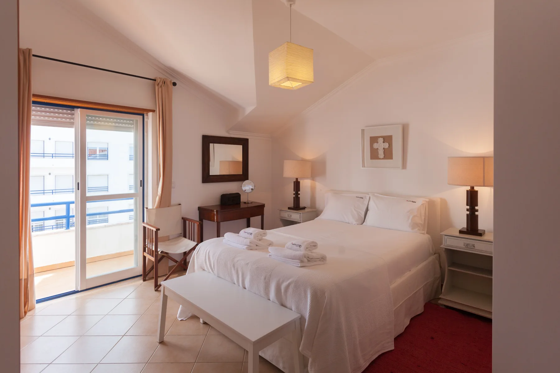 Un dormitorio luminoso con una cama grande, mesillas y una puerta acristalada que da a un balcón.