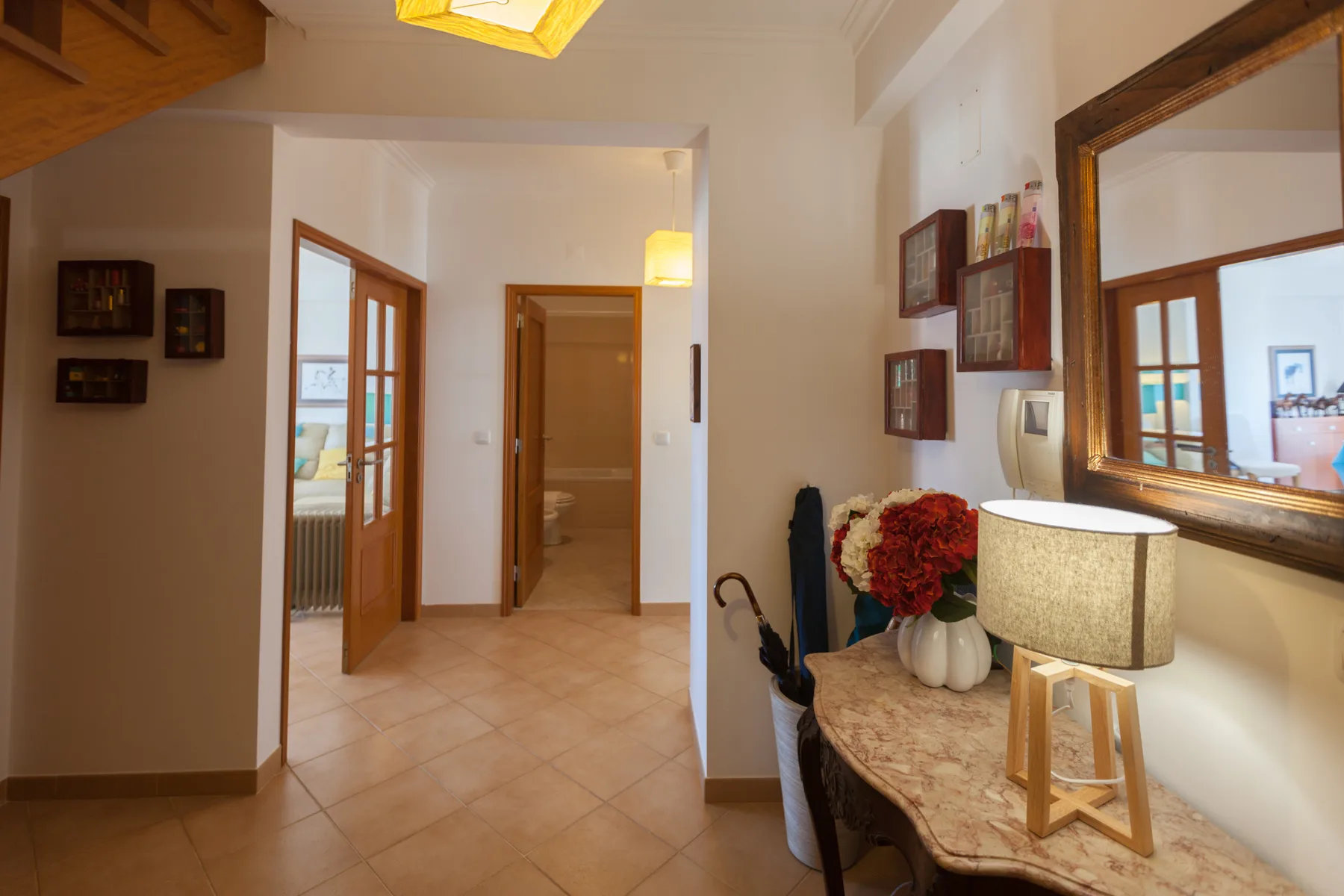An apartment hallway with tiled flooring, wooden doorways, and a console table.