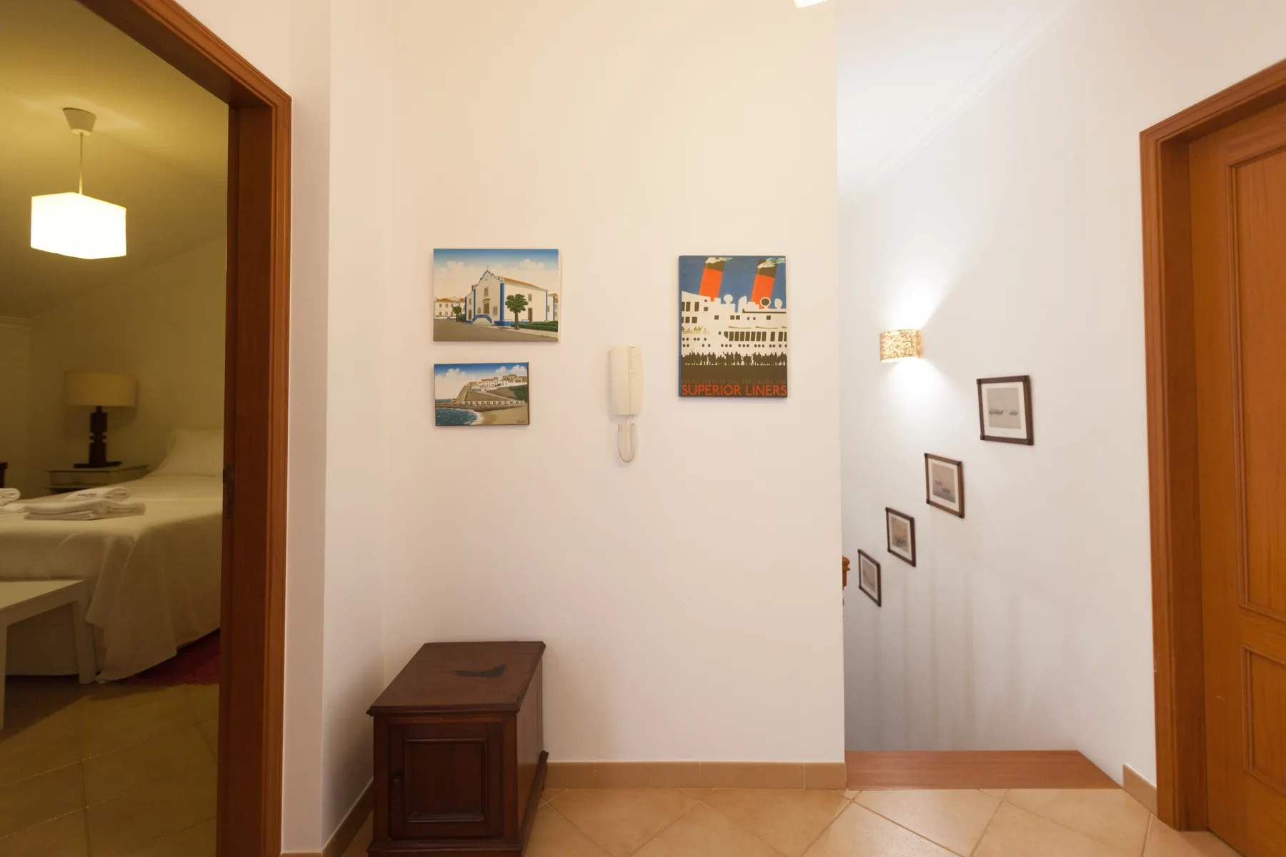 A hallway with framed pictures, a small wooden cabinet, and doorways.