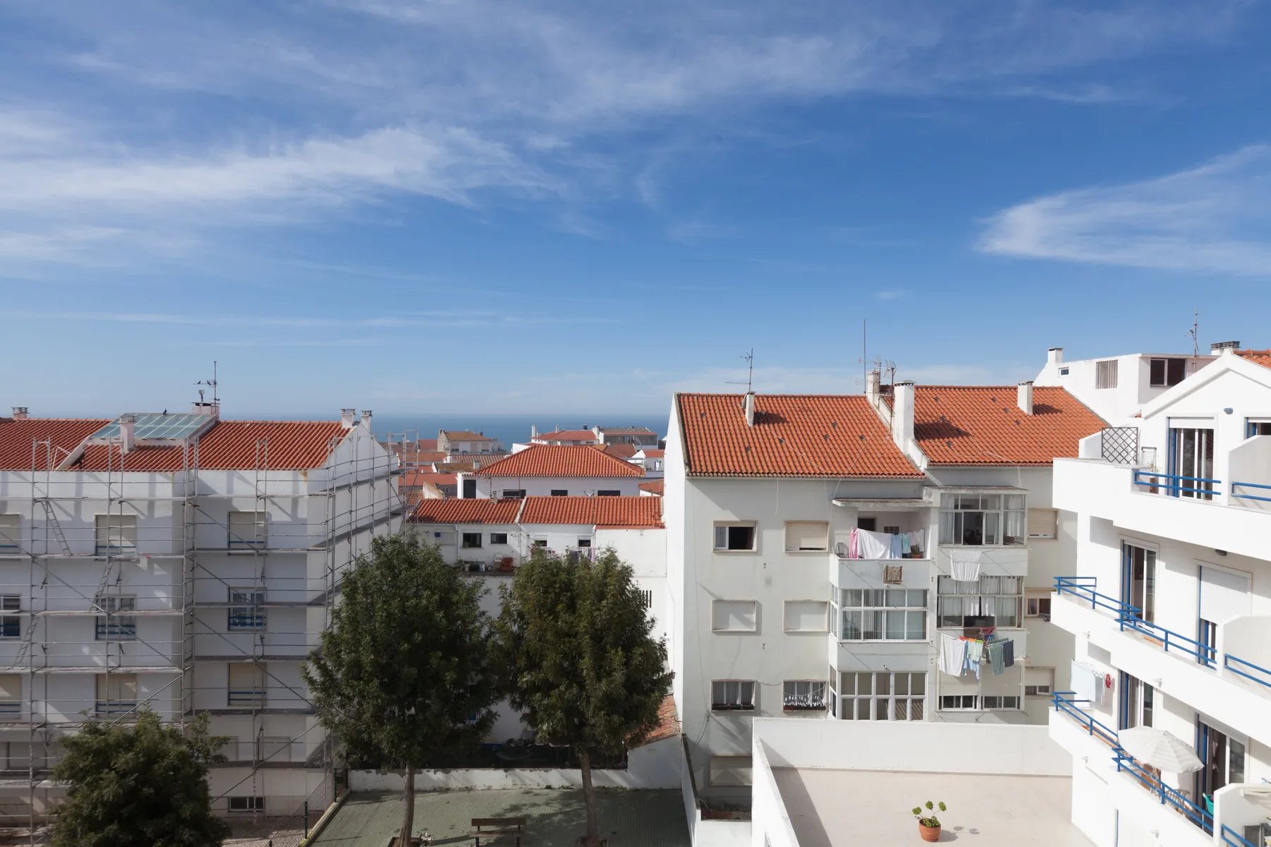 A coastal town view shows clustered buildings with red-tiled roofs beneath a blue sky.