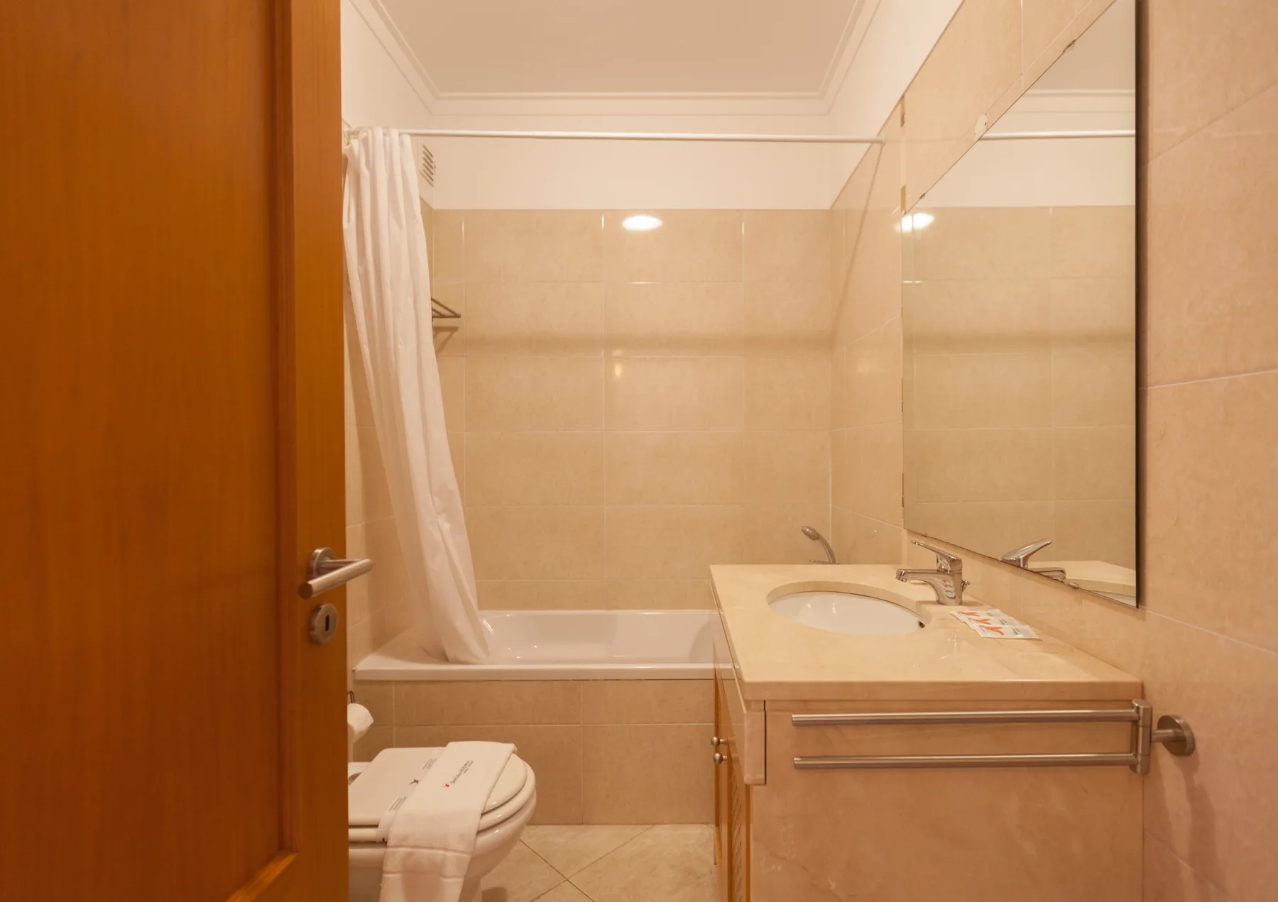A bathroom with a bathtub, shower curtain, and sink beside a large mirror.