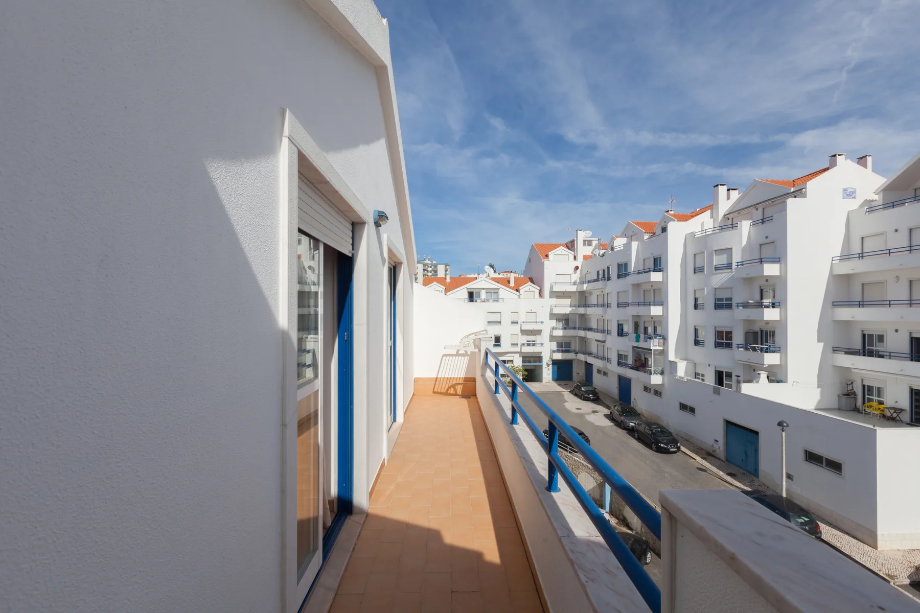 A sunny balcony overlooks white buildings along a residential street.