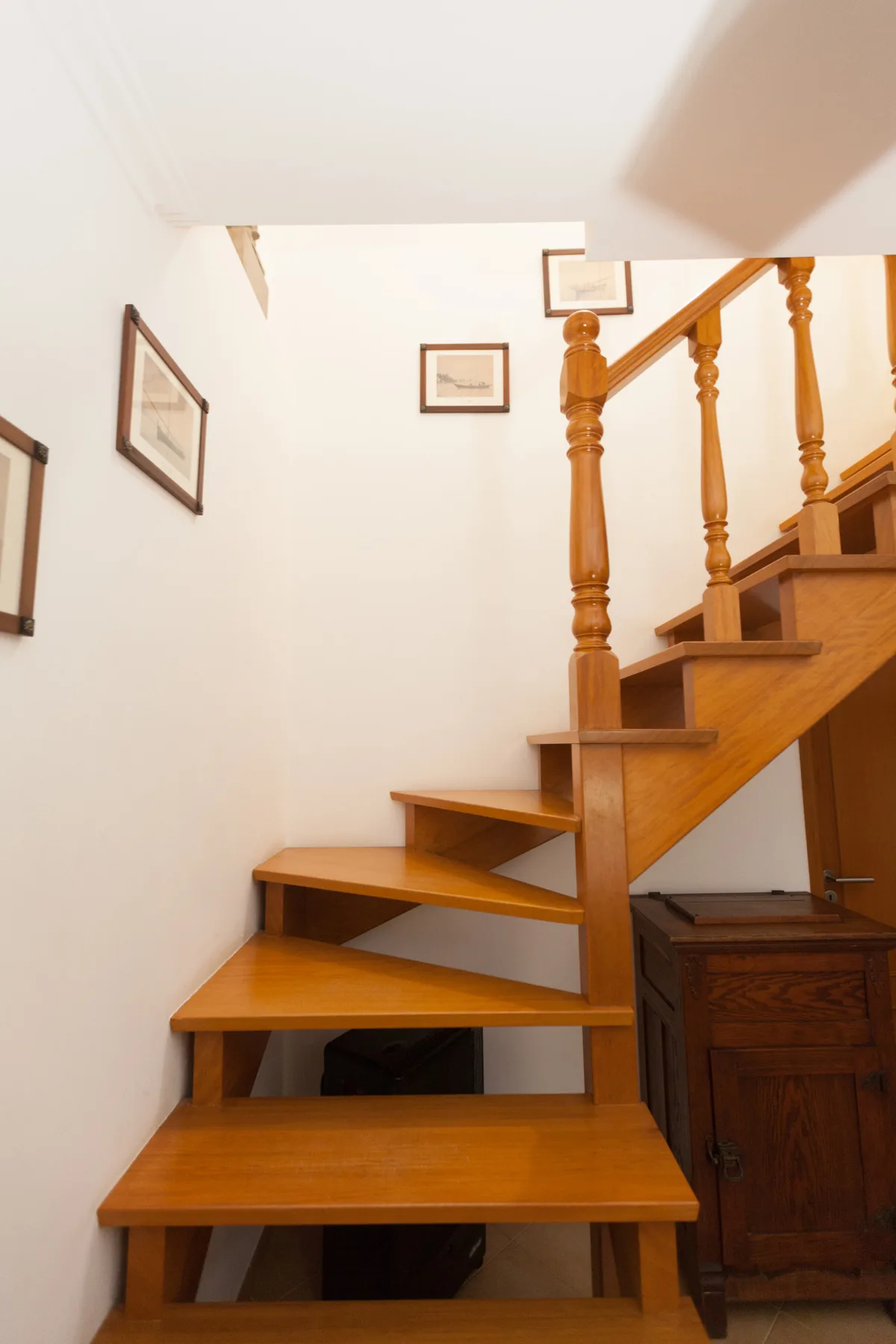 An interior staircase with wooden steps rises beside a white wall.