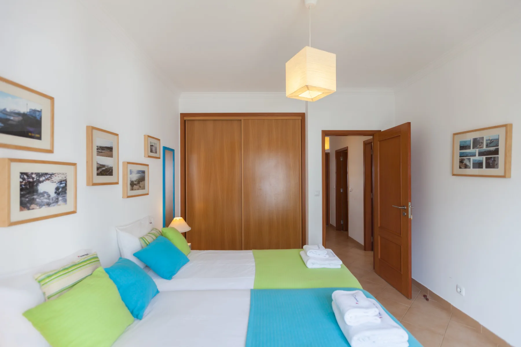 A bedroom with two beds, colorful pillows, and framed pictures on the walls.