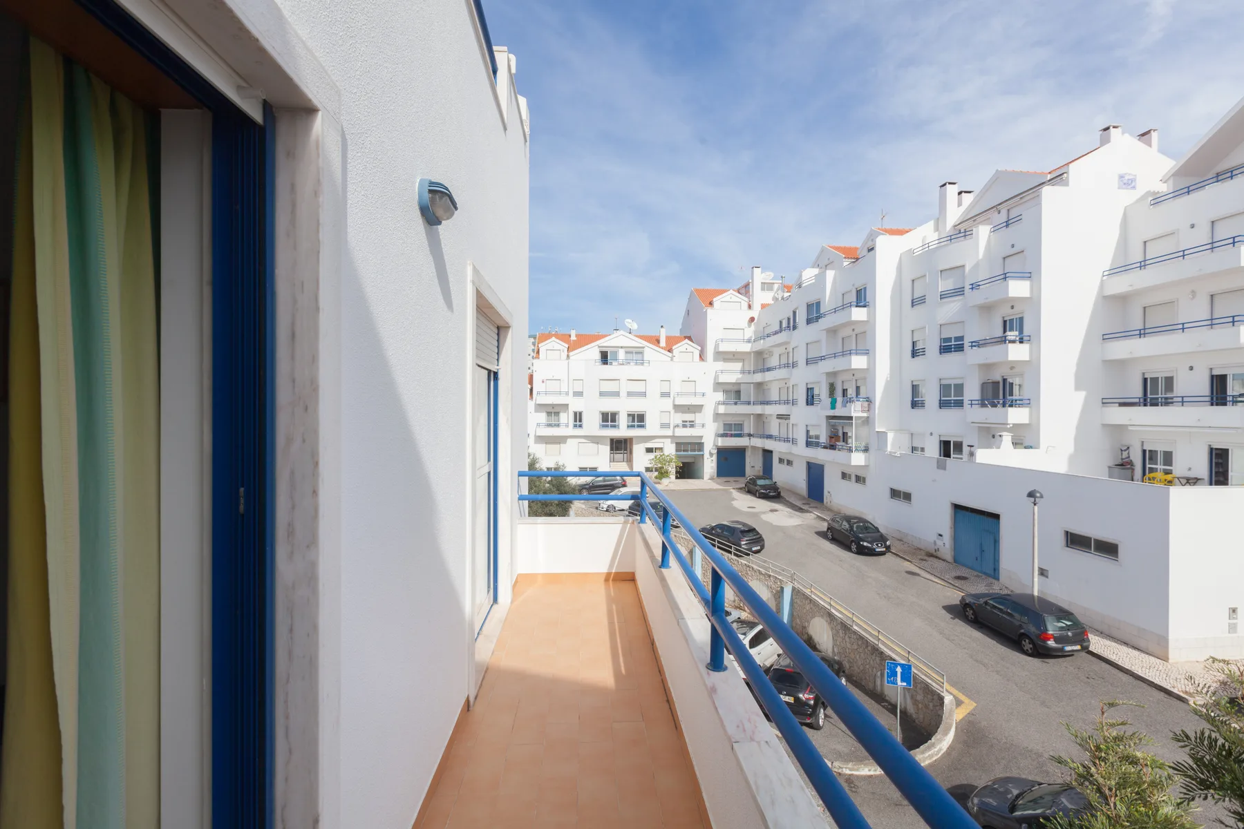 A narrow balcony overlooks a street lined with white apartment buildings.