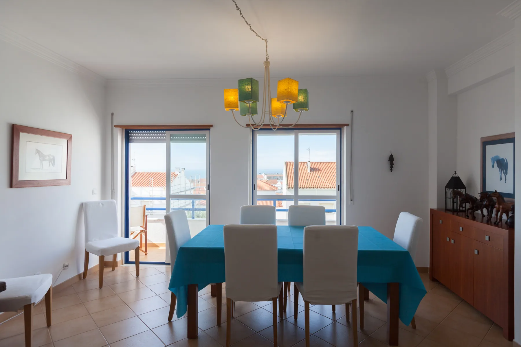 A dining room with a table set near windows overlooking rooftops.