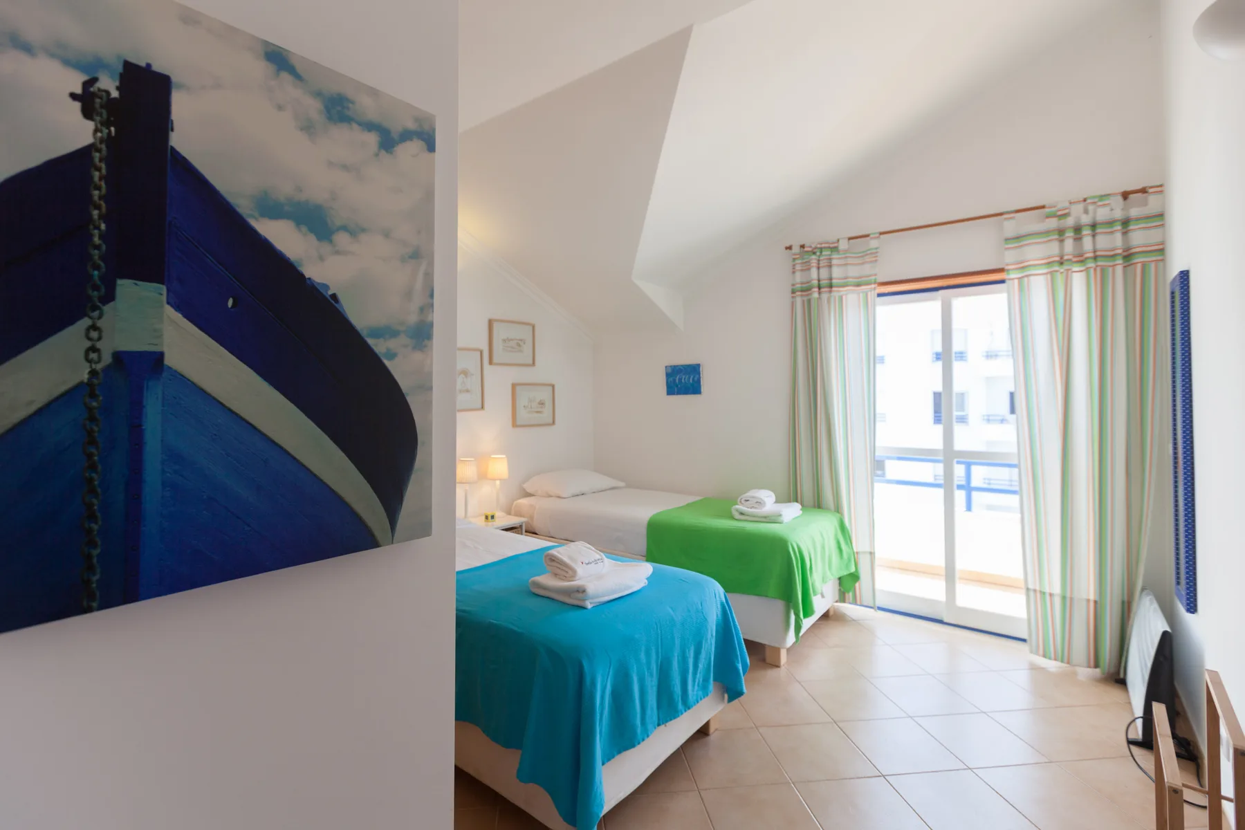 A bright bedroom with two beds beside a glass balcony door.