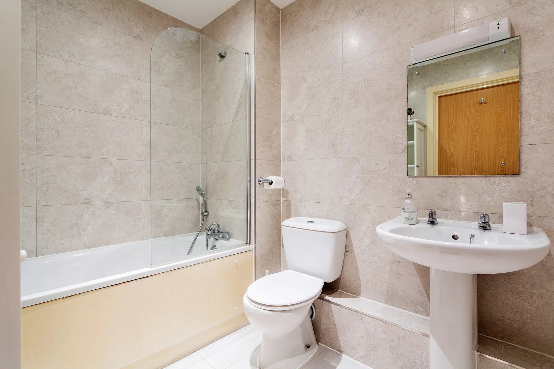 Un baño alicatado con bañera, inodoro y lavabo con pedestal.