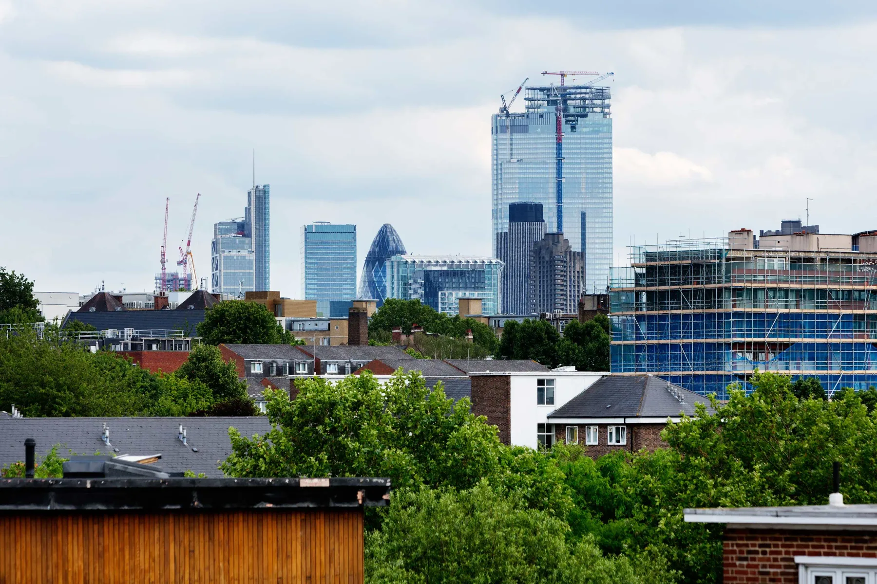 Panorámica urbana con edificios altos modernos tras tejados y árboles.