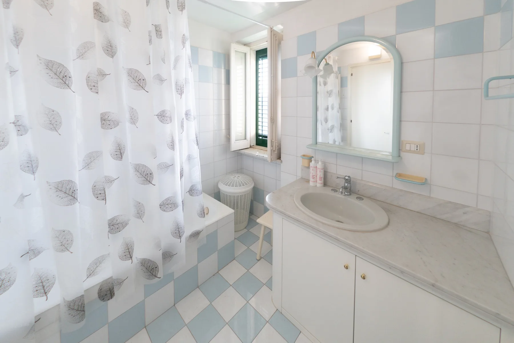 Un baño alicatado con lavabo, espejo y cortina de ducha estampada.