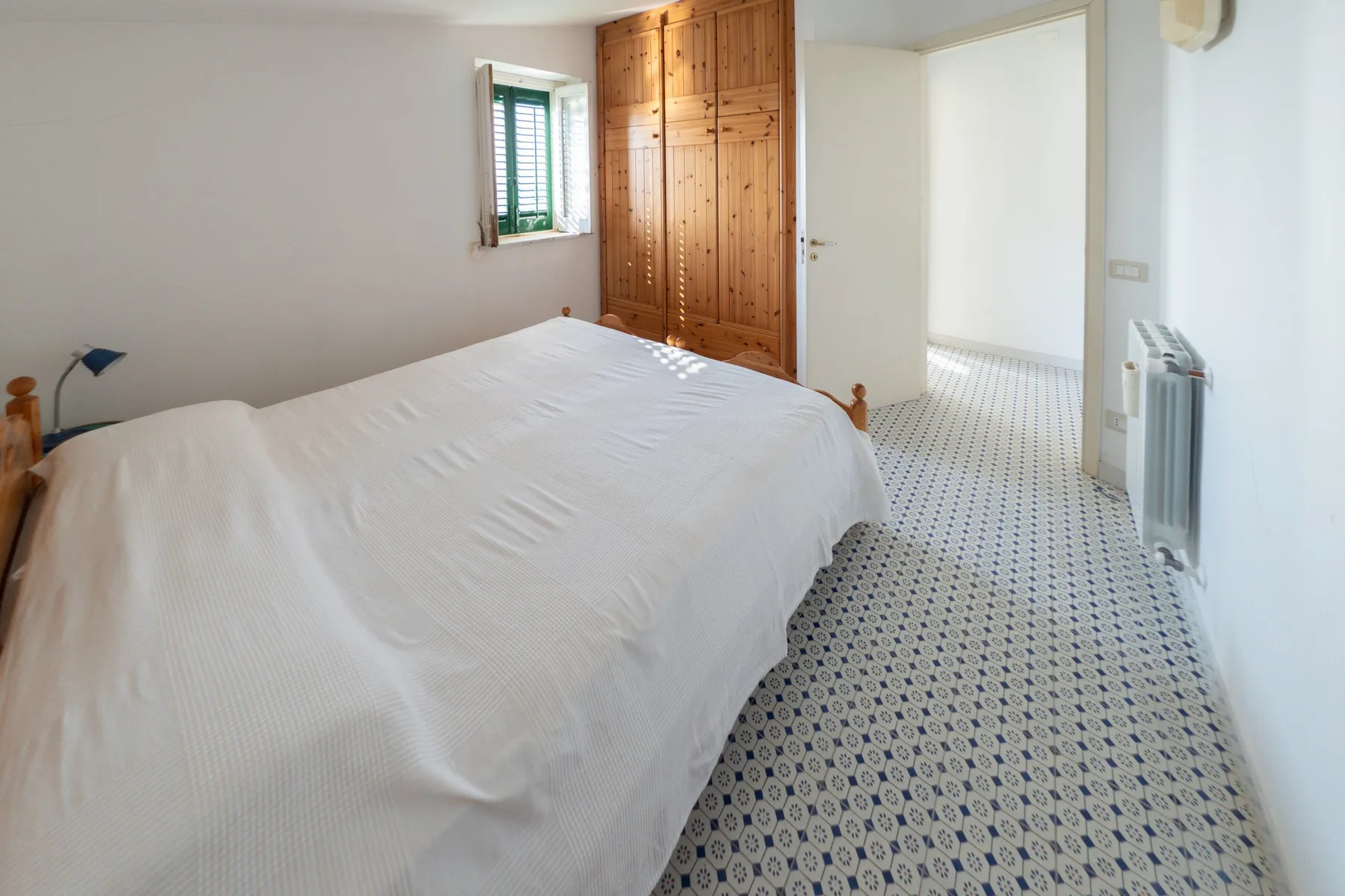 Un dormitorio con una cama blanca, un armario de madera y un suelo estampado.
