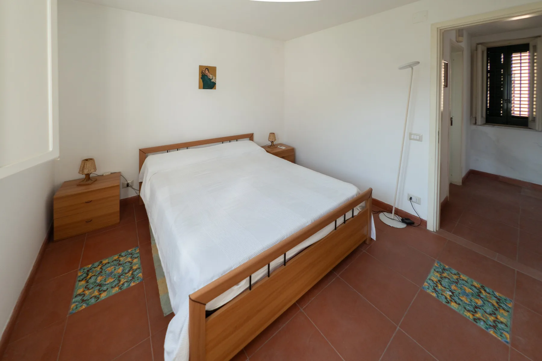 Un dormitorio con una cama de madera, mesitas de noche y suelo de baldosas.