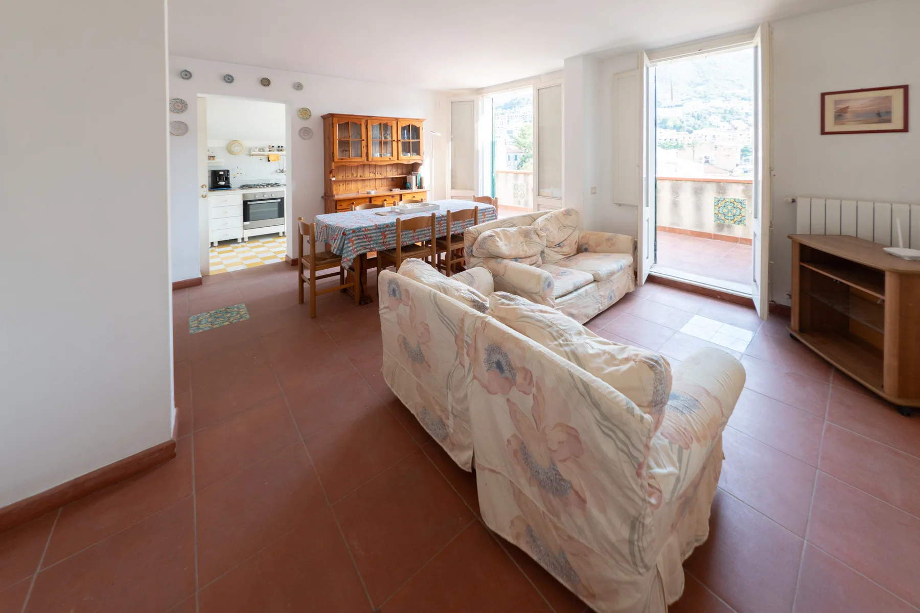 Una sala y comedor con asientos tapizados, una mesa de comedor y una luminosa puerta al balcón.