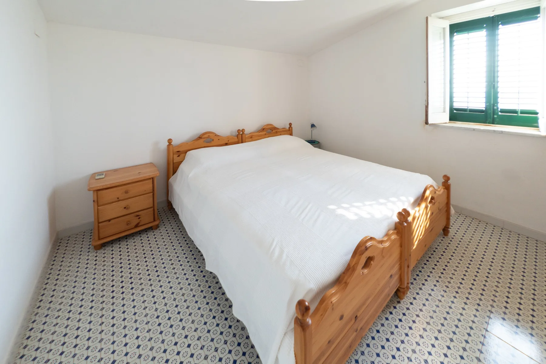 A bedroom with a wooden bed, a bedside cabinet, and a window.