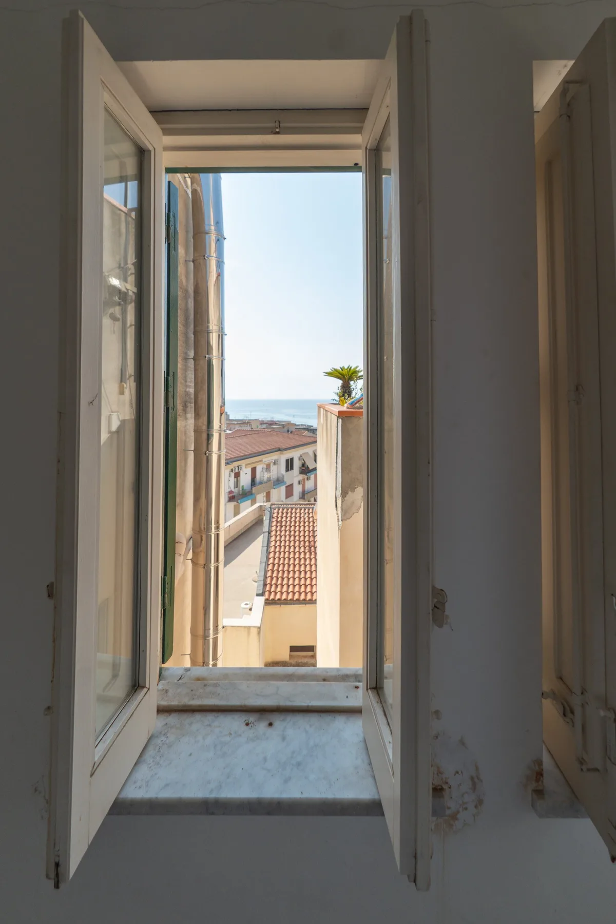 Una ventana abierta da a los tejados cercanos y al mar.