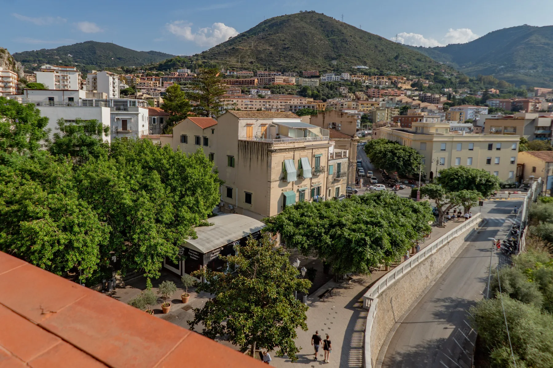 Un pueblo en la ladera con edificios agrupados, árboles y una montaña al fondo.