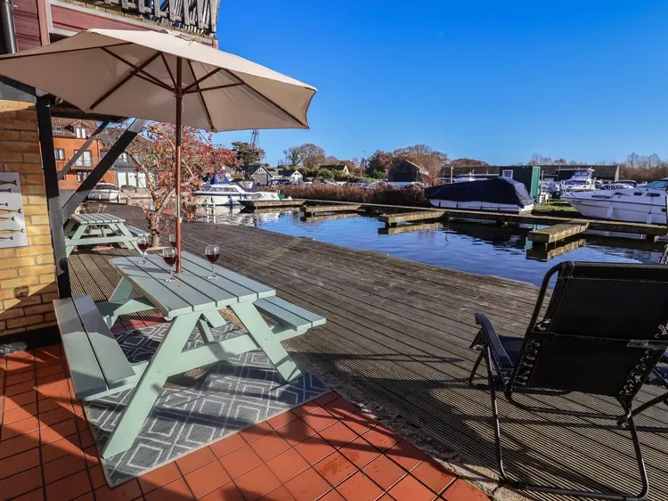 A waterside deck with picnic seating overlooks a marina filled with boats.