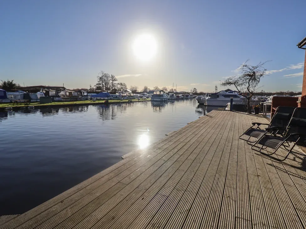 Un muelle soleado se extiende junto a aguas tranquilas y barcos amarrados.