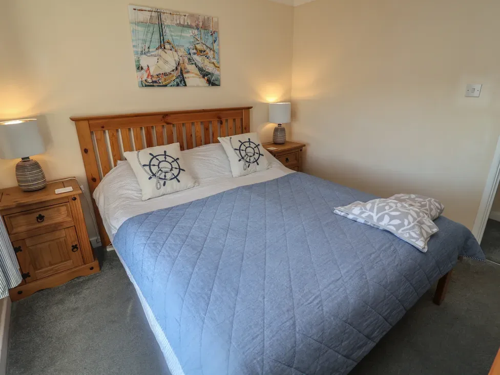 Un dormitorio con una cama de madera, ropa de cama azul y mesitas a juego.