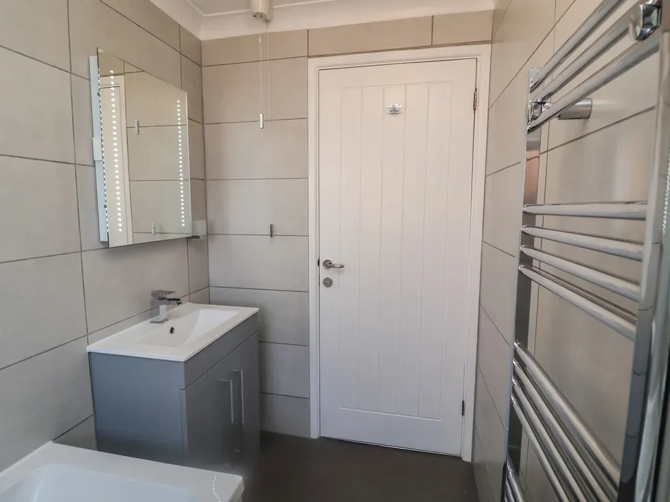 Un baño alicatado con lavabo, espejo y radiador toallero.