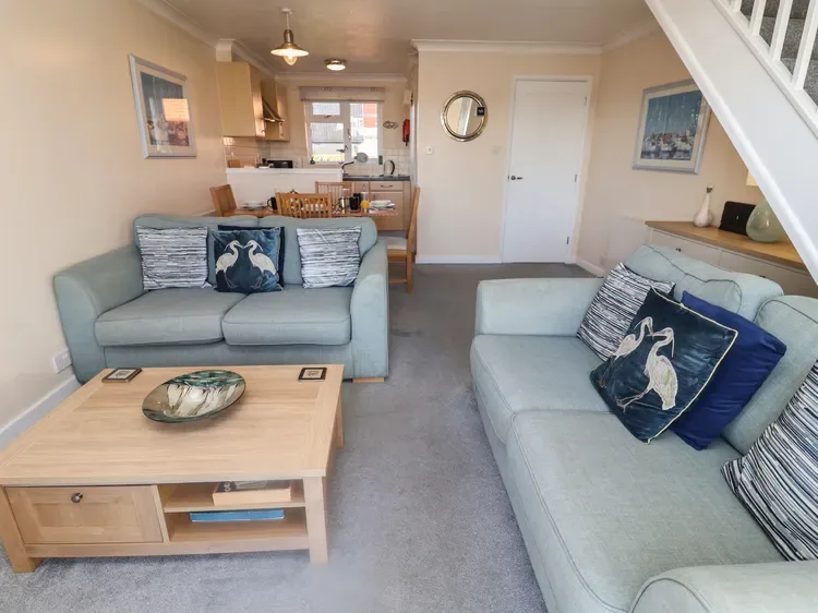A living room with two seating areas and a coffee table, opening onto a kitchen.