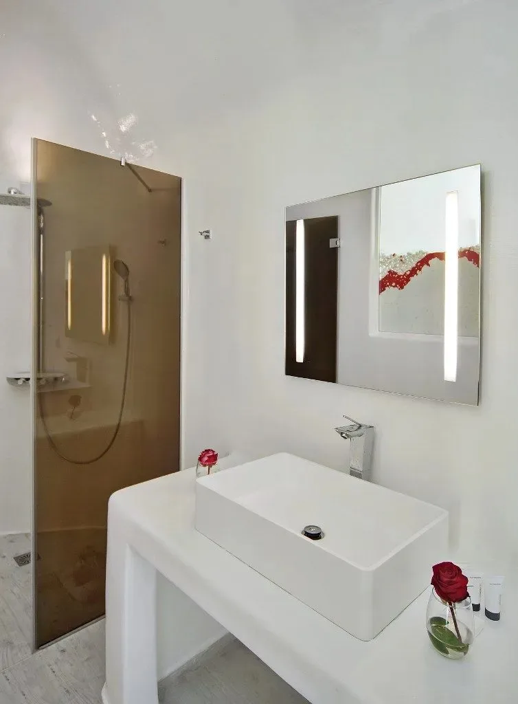 Un baño luminoso con un lavabo sobre encimera blanco junto a una ducha de vidrio.