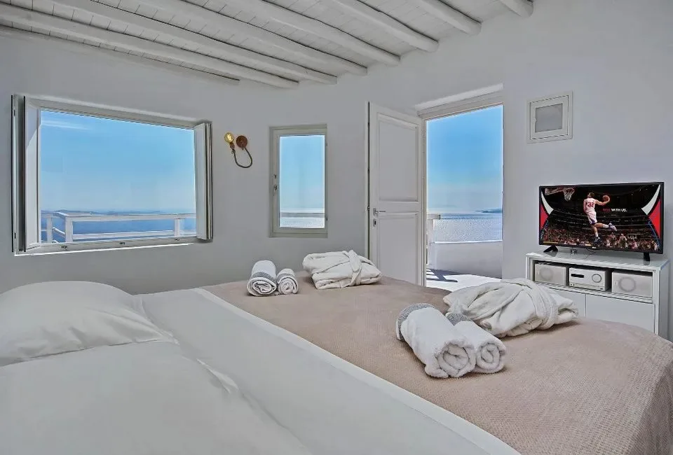 Un dormitorio luminoso con camas, toallas dobladas y ventanas con vistas al mar.