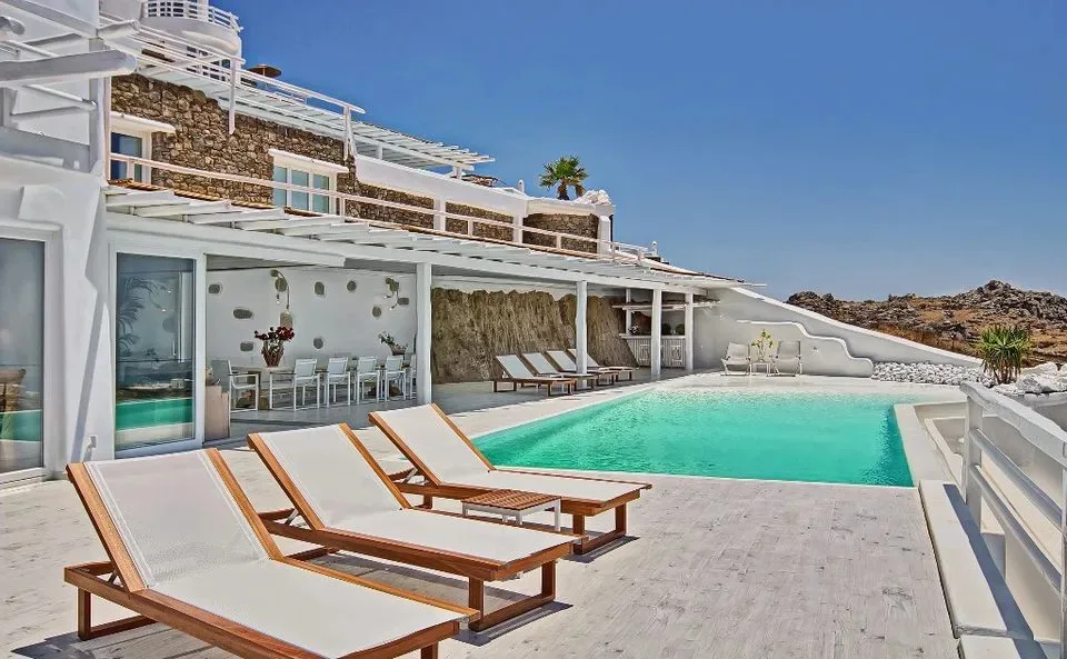An outdoor swimming pool with lounge chairs beside a white terrace.